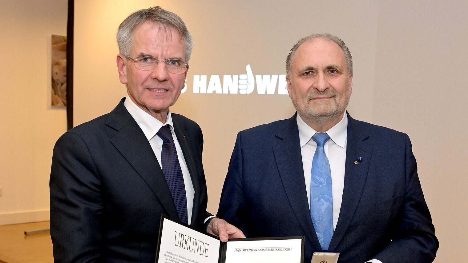 Andreas Ehlert und Hans Peter Wollseifer posieren für ein Pressefoto. Sie zeigen die Urkunde und die Goldene Medaille.