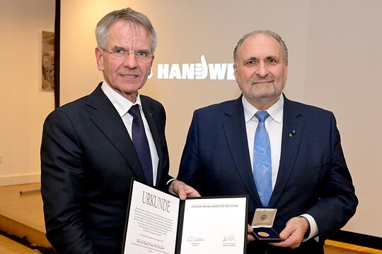 Andreas Ehlert und Hans Peter Wollseifer posieren für ein Pressefoto. Sie zeigen die Urkunde und die Goldene Medaille.