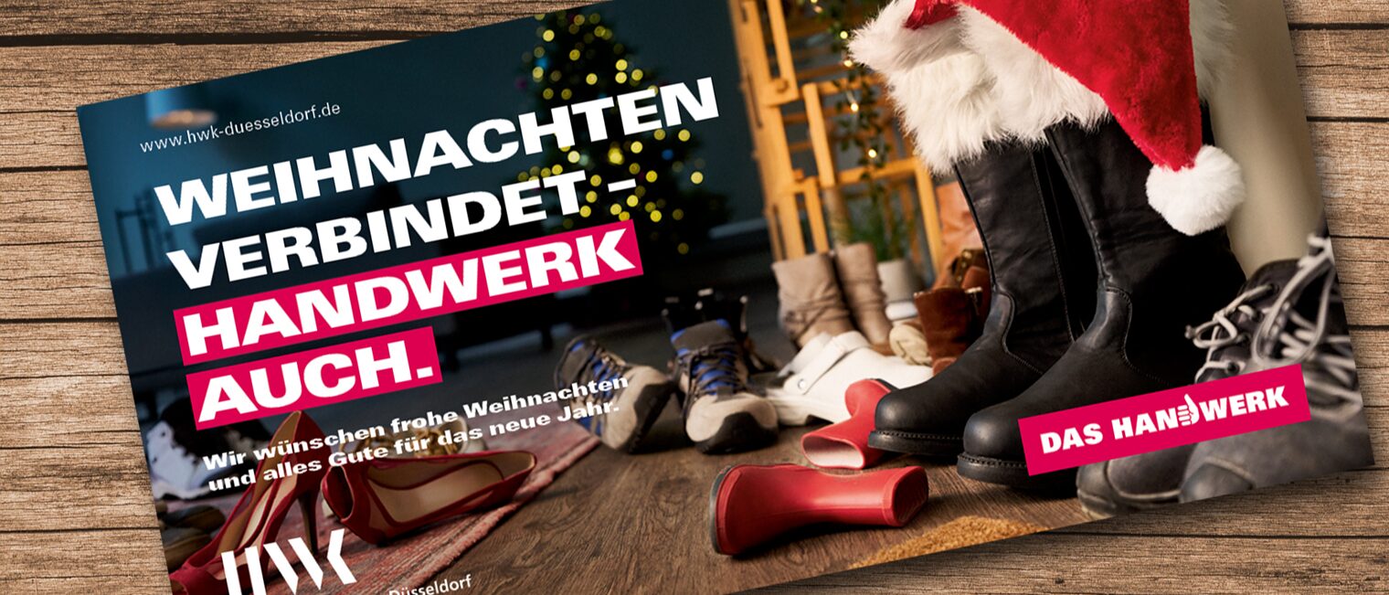 Eine Weihnachtskarte liegt auf einem Holz-Untergrund. Eine Weihnachtsmann-Mütze steckt in Winterstiefeln.Text: Weihnachten verbindet. Handwerk auch". 