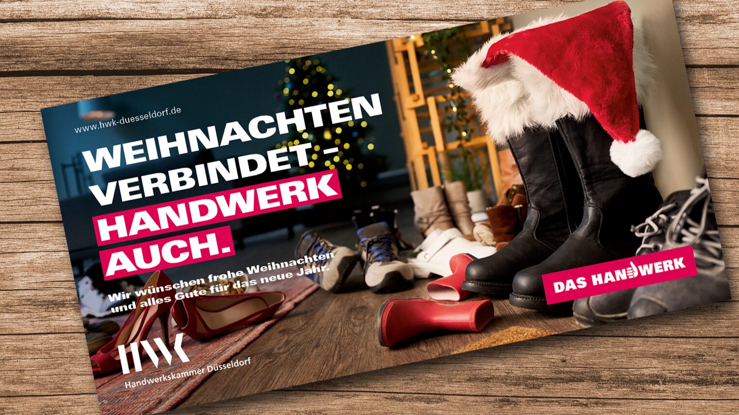 Eine Weihnachtskarte liegt auf einem Holz-Untergrund. Eine Weihnachtsmann-Mütze steckt in Winterstiefeln.Text: Weihnachten verbindet. Handwerk auch". 