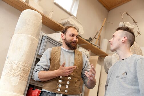 Steinmetz-Ausbilder spricht mit Azubi in Werkstatt.