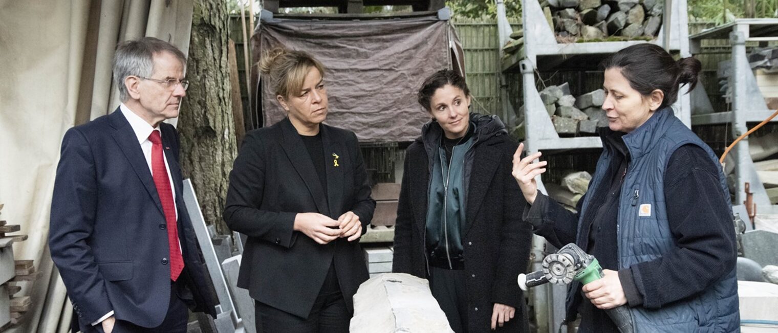 Die Teilnehmenden sprechen mit Steinbildhauermeisterin Anna Staudt. Im Vordergrund ist ein Stein-Rohling zu sehen.