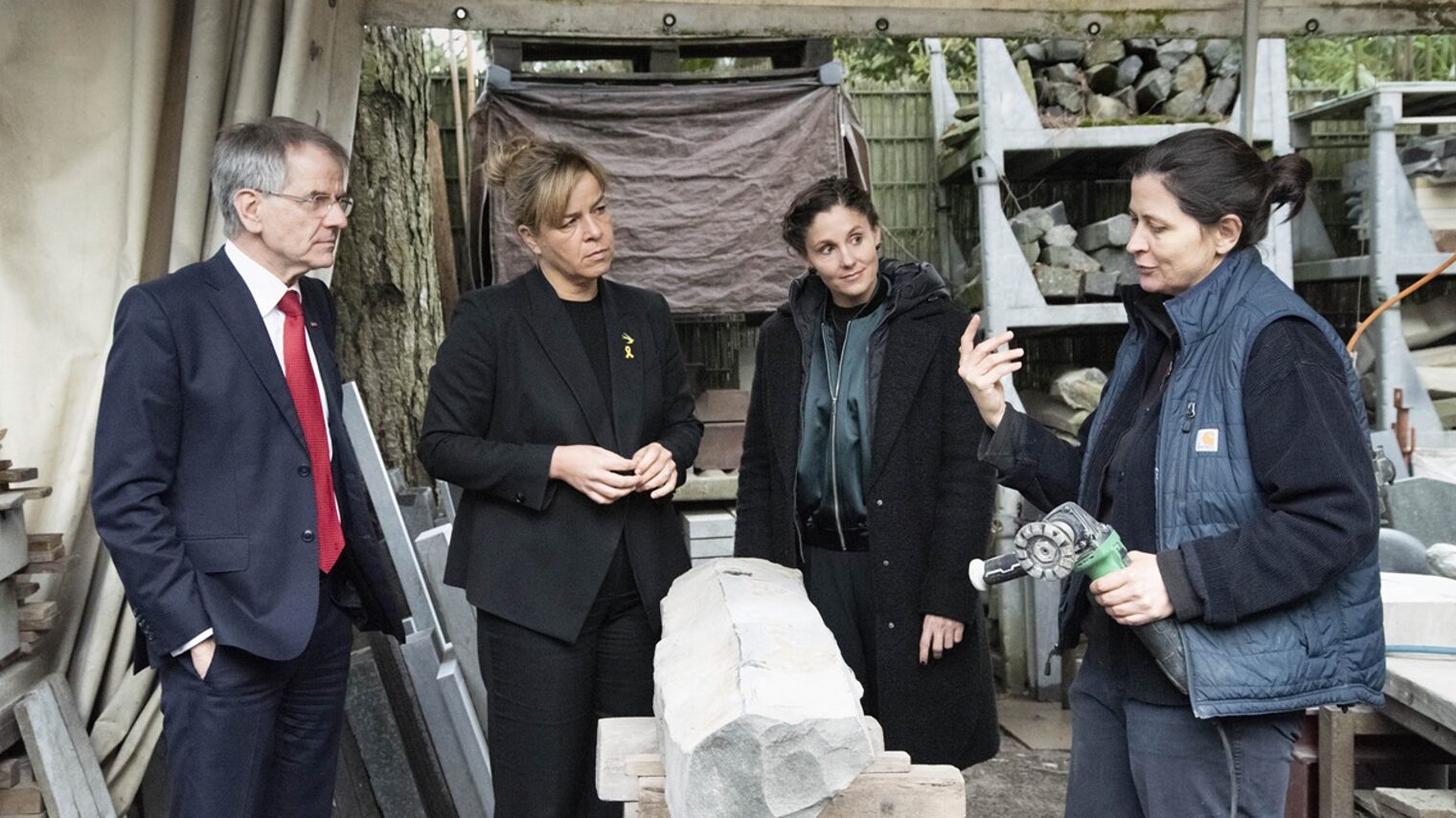 Die Teilnehmenden sprechen mit Steinbildhauermeisterin Anna Staudt. Im Vordergrund ist ein Stein-Rohling zu sehen.