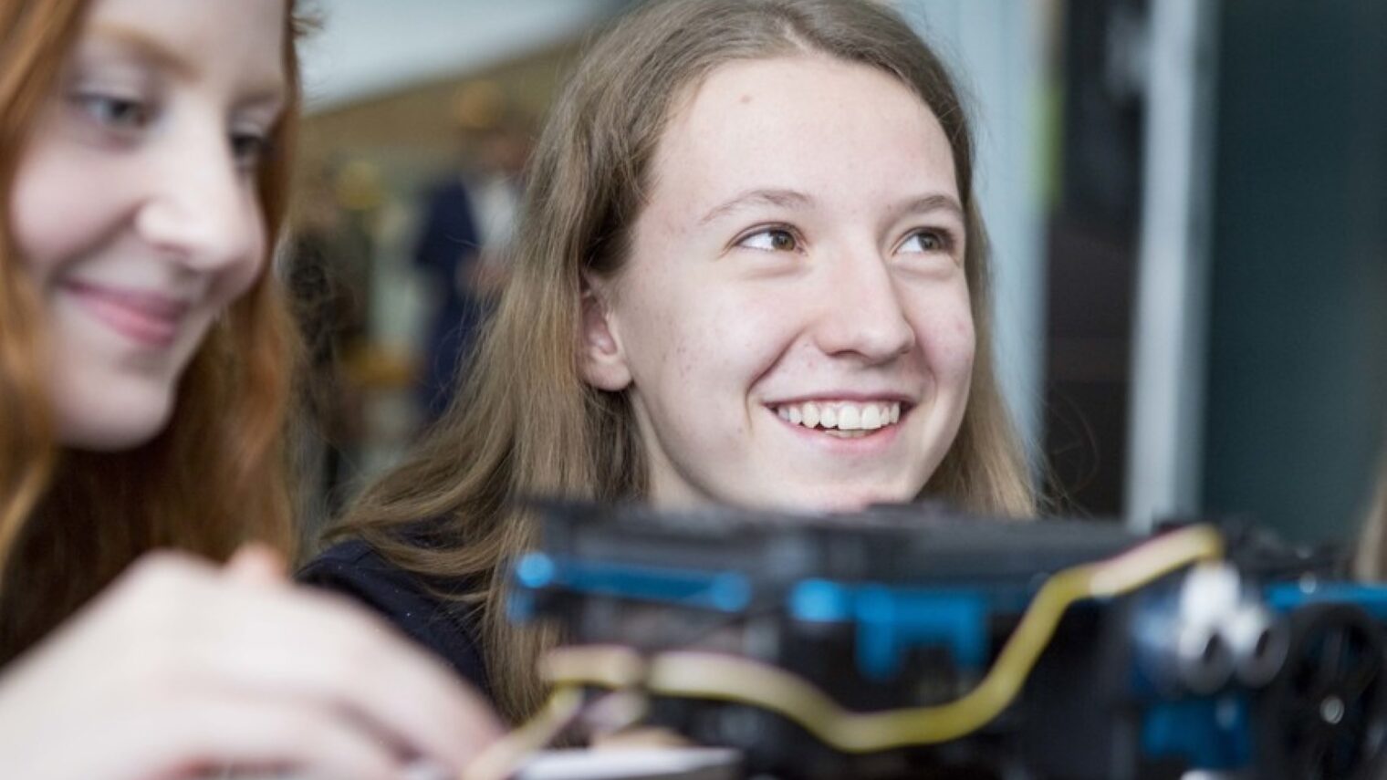 Nahaufnahme von zwei lächelnden Mädchen vor einer technischen Apparatur 