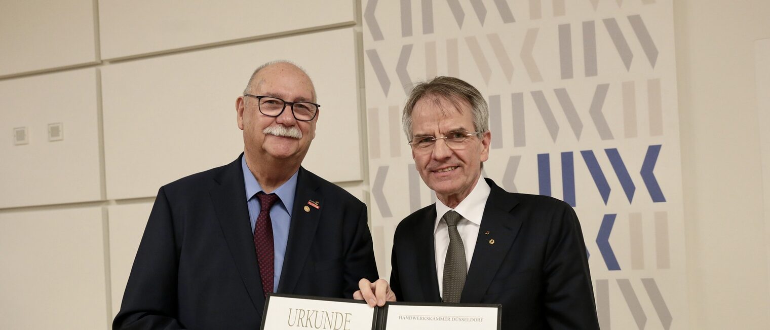 Bernd Münzenhofer und Andreas Ehlert posieren für ein Pressefoto. Sie zeigen die Urkunde, die Bernd Münzenhofer erhalten hat.