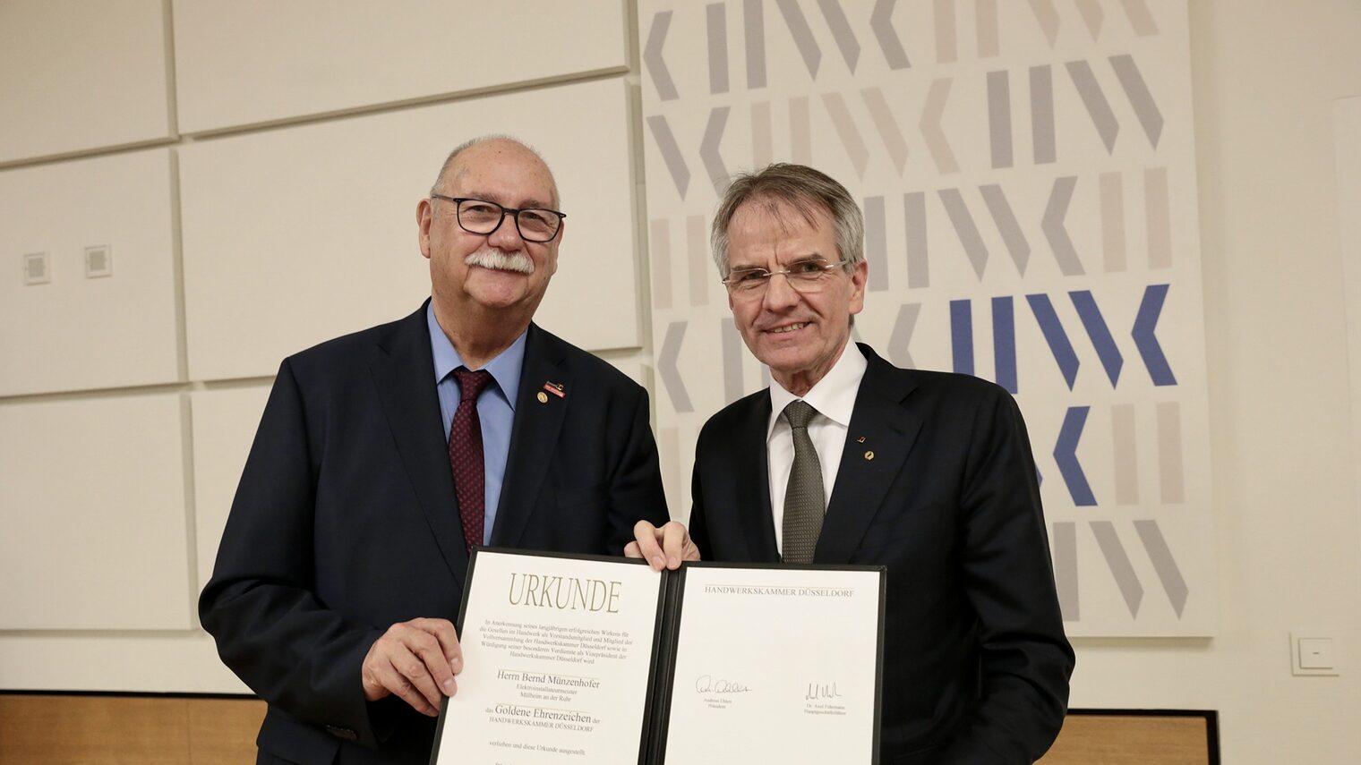 Bernd Münzenhofer und Andreas Ehlert posieren für ein Pressefoto. Sie zeigen die Urkunde, die Bernd Münzenhofer erhalten hat.