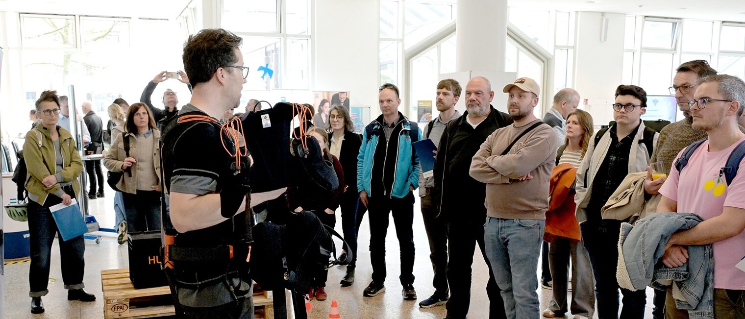 Ein Aussteller der Messe "Exoskelette und praktische Hilfsmittel für den Betriebsalltag" zeigt die Unterstützung beim Heben und Tragen von Lasten vor Publikum in der Handwerkskammer Düsseldorf.
