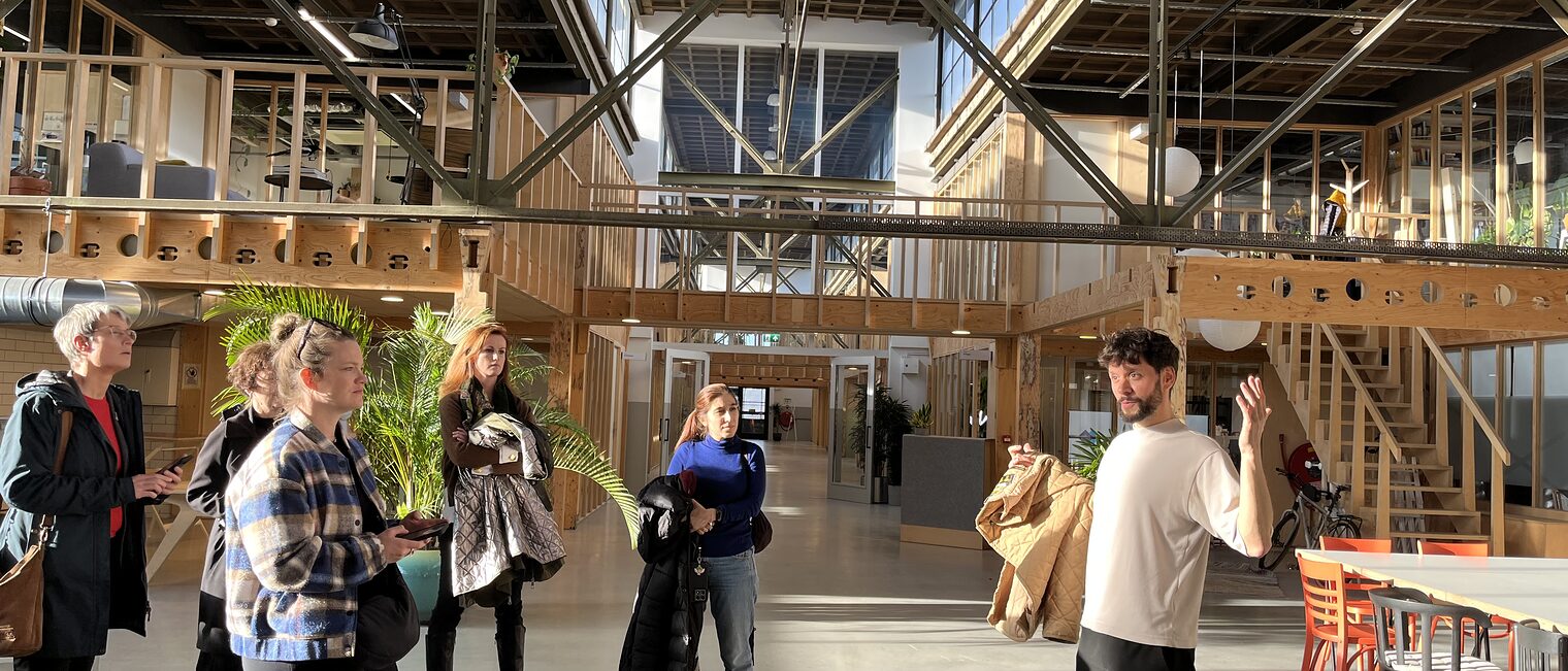 Gruppe junger Menschen steht in der Halle eines Holzbaus und lässt sich die Vorteile des nachhaltigen Bauens erklären. 