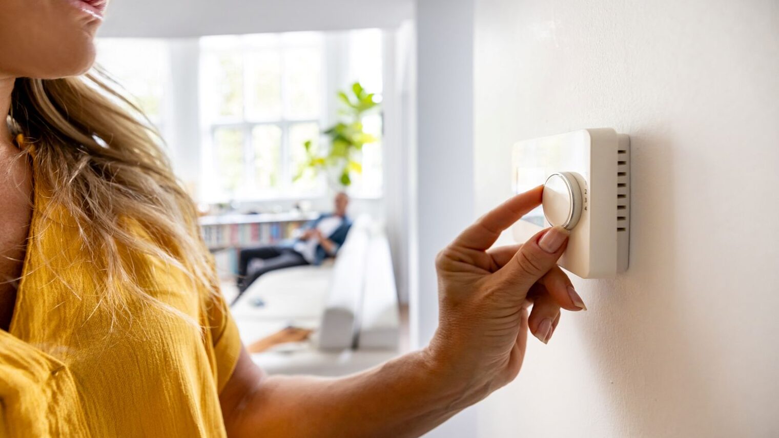 Eine Frau stellt in ihrer Wohnung die Temperatur am Heizungsregler ein.