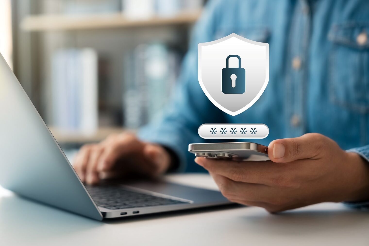 Ein Mann arbeitet am Laptop mit Smartphone in der einen Hand. Eingebunden ist ein Schloss-Symbol für Cybersicherheit.