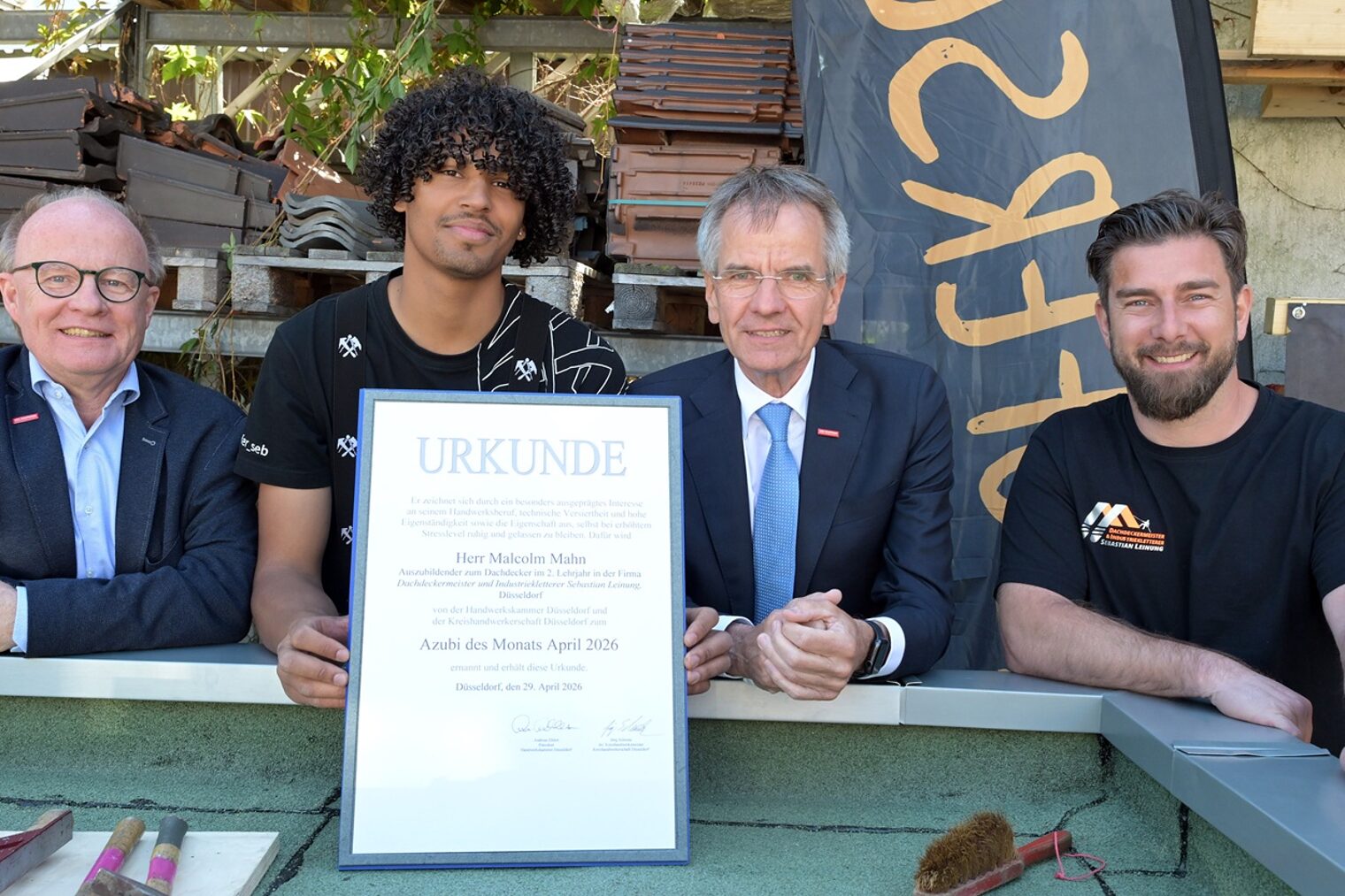 4 Personen posieren für ein Pressefoto. Der frisch ausgezeichnete Azubi des Monats zeigt seine Urkunde.