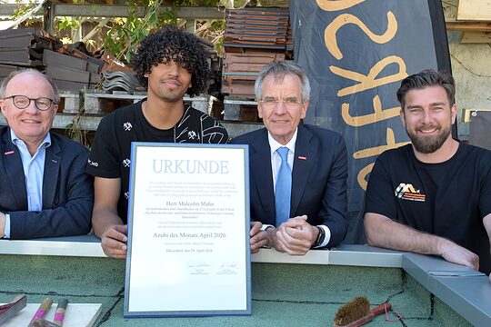 4 Personen posieren für ein Pressefoto. Der frisch ausgezeichnete Azubi des Monats zeigt seine Urkunde.