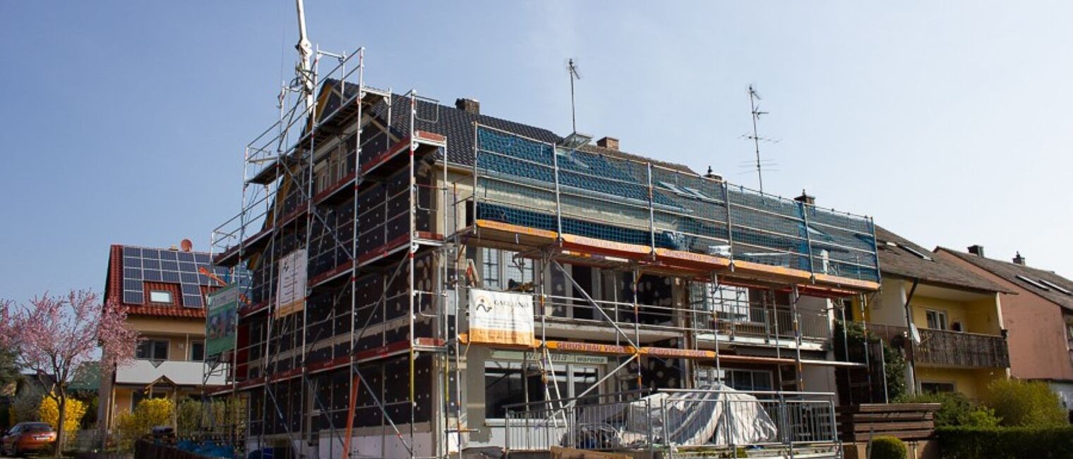 Auf dem Bild ist ein Haus von außen zu sehen, welches gerade modernisiert wird. Das Haus ist von einem Baugerüst umgeben.