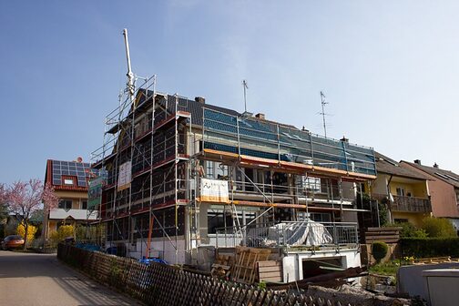 Auf dem Bild ist ein Haus von außen zu sehen, welches gerade modernisiert wird. Das Haus ist von einem Baugerüst umgeben.