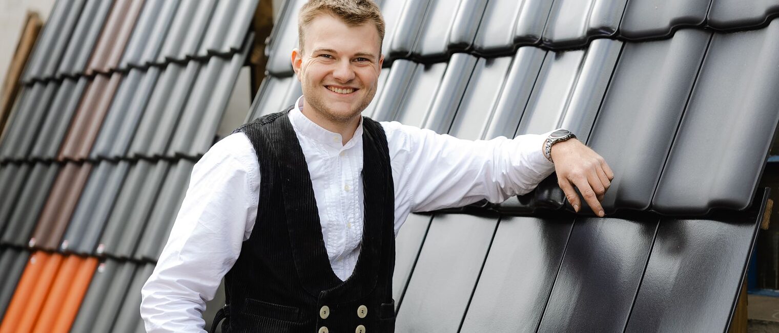 Jonah Zittlau, Dachdecker, lehnt entspannt an einer Wand aus Dachpfannen.