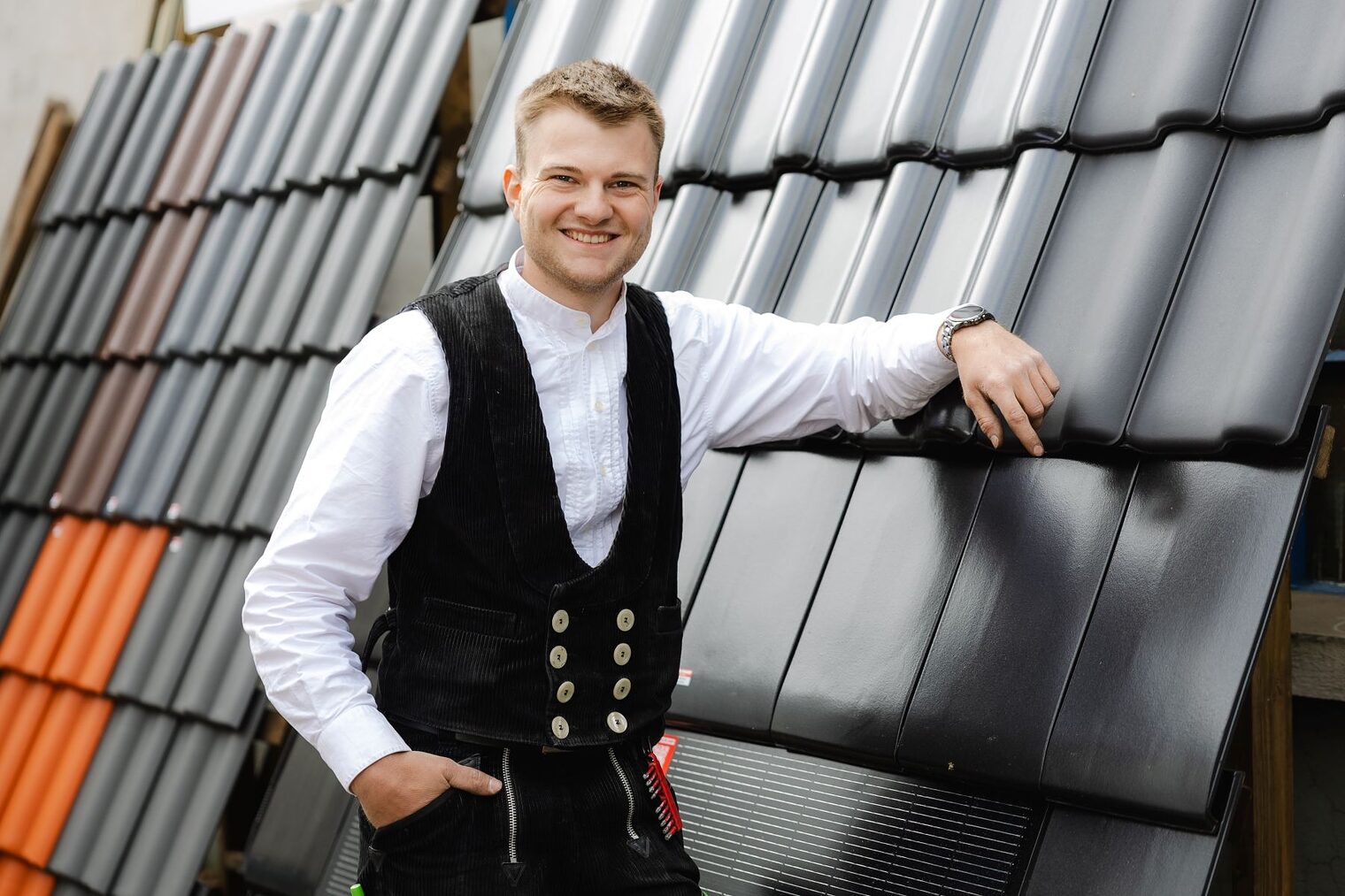 Jonah Zittlau, Dachdecker, lehnt entspannt an einer Wand aus Dachpfannen.