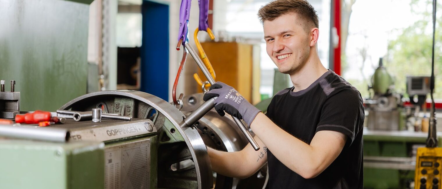 Moritz Jordan steht an einer Werkmaschine und lächelt in die Kamera