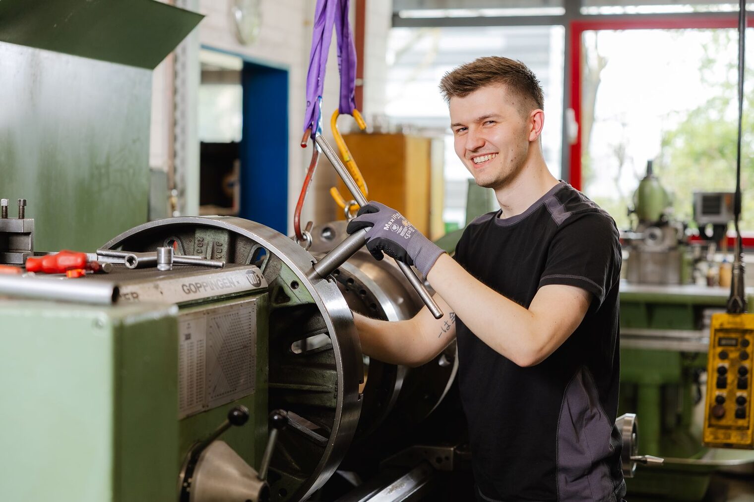 Moritz Jordan steht an einer Werkmaschine und lächelt in die Kamera