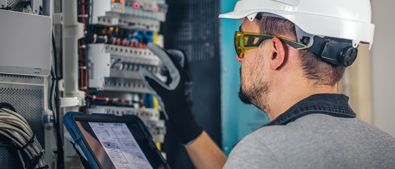 Ein Elektrotechniker oder Installateur arbeitet mit einem Tablet an einer Schalteinheit mit Sicherungen.