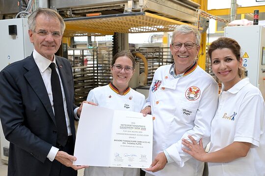 Die Preisträgerin posiert mit drei weiteren Personen für ein Pressefoto. Sie präsentieren die Urkunde.