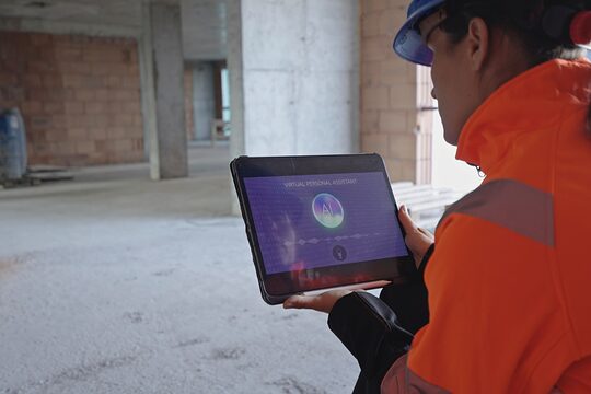 Handwerkerin oder Architektin arbeitet mit Tablet und KI in einem Rohbau einer Baustelle.