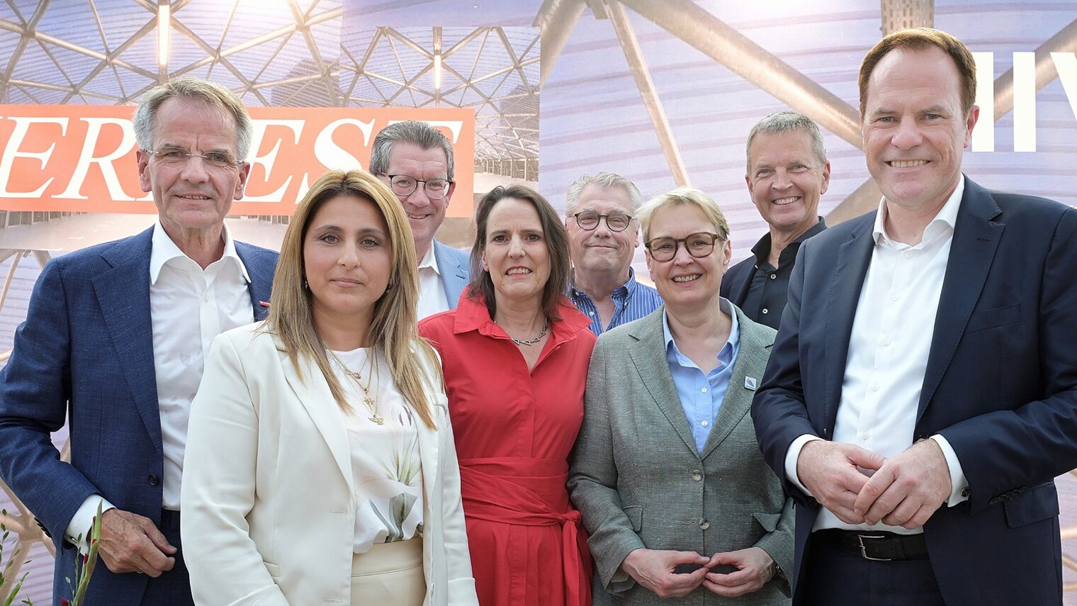 Mehrere Teilnehmende posieren vor einem Hintergrund mit der Schrift Sommerfest für ein Pressefoto.