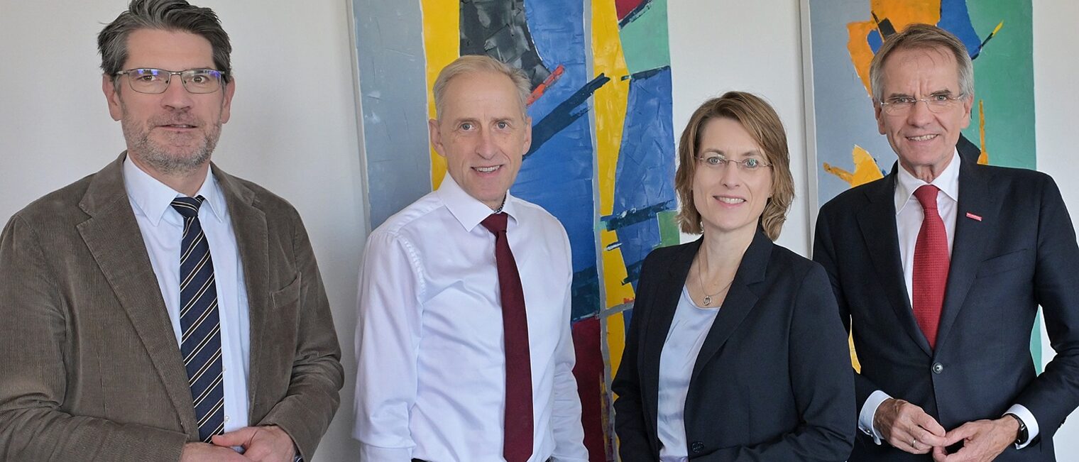 Drei Funktionäre aus dem Handwerk posieren mit Frau Garbade für ein Pressefoto. Im Hintergrund sind zwei bunte Bilder zu sehen.