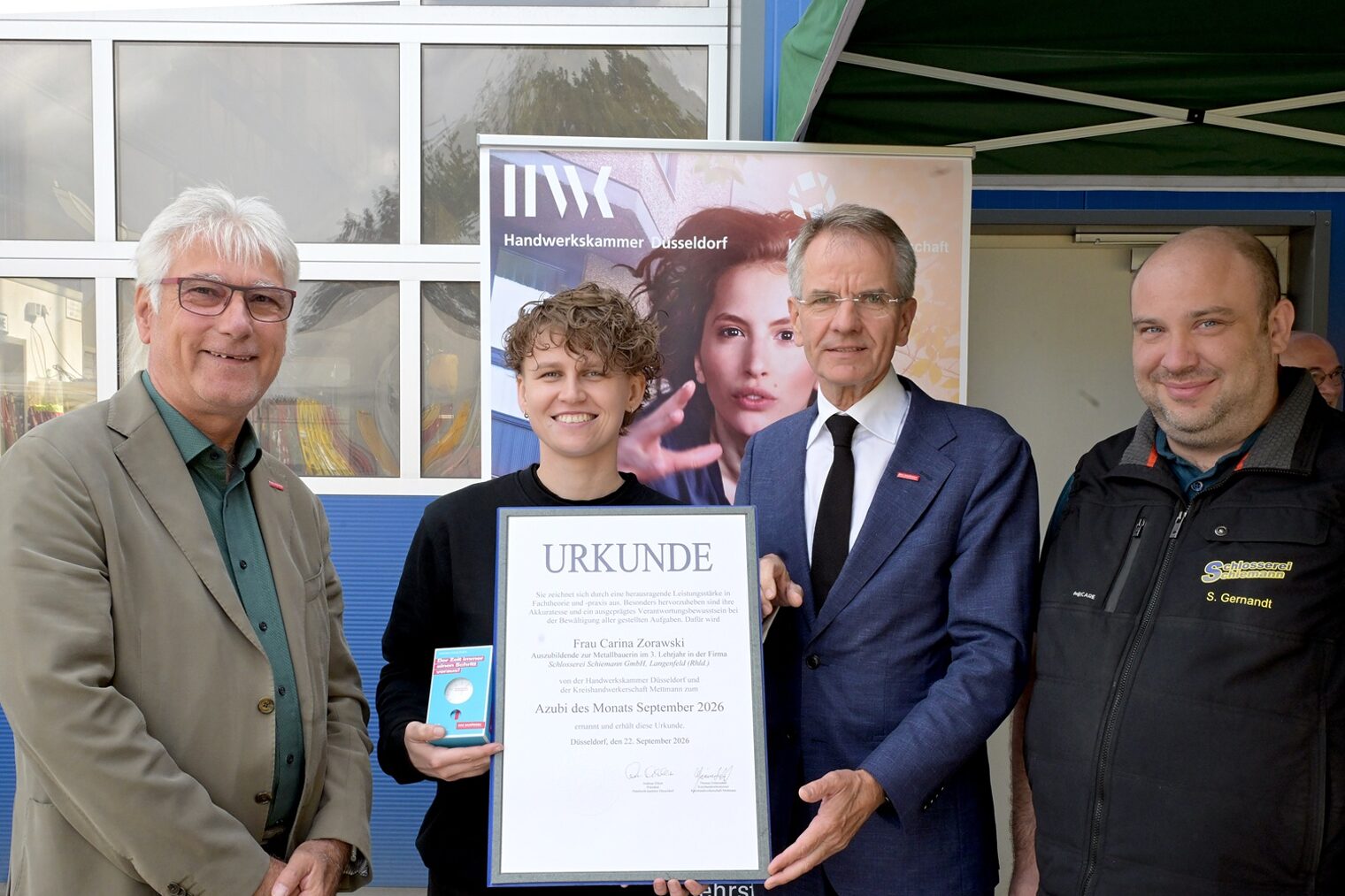Carina Zorawski posiert mit 3 Handwerksfunktionären für ein Pressefoto. Sie zeigt ihre Auszeichnungsurkunde und eine Uhr.
