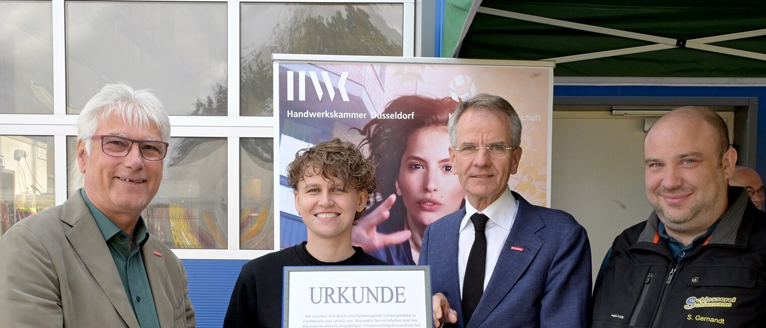 Carina Zorawski posiert mit 3 Handwerksfunktionären für ein Pressefoto. Sie zeigt ihre Auszeichnungsurkunde und eine Uhr.